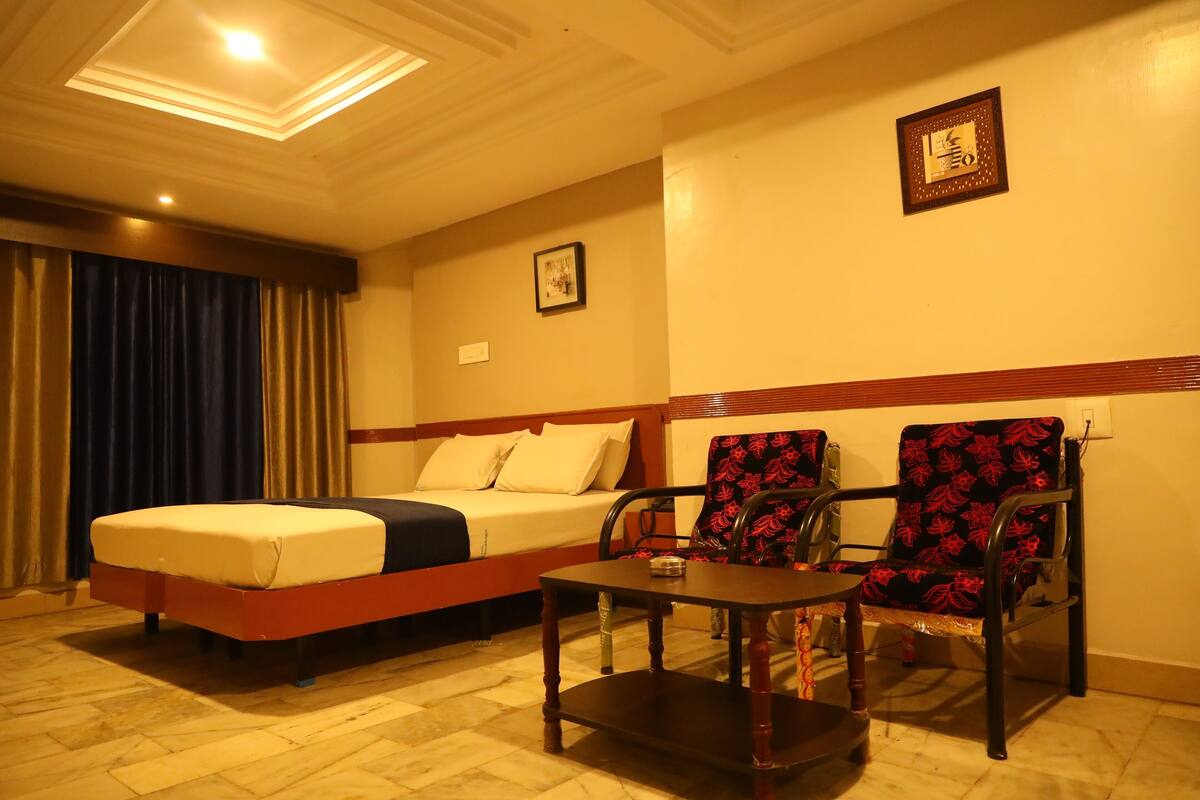 A hotel room with a bed, two chairs, a small table, and a ceiling light.