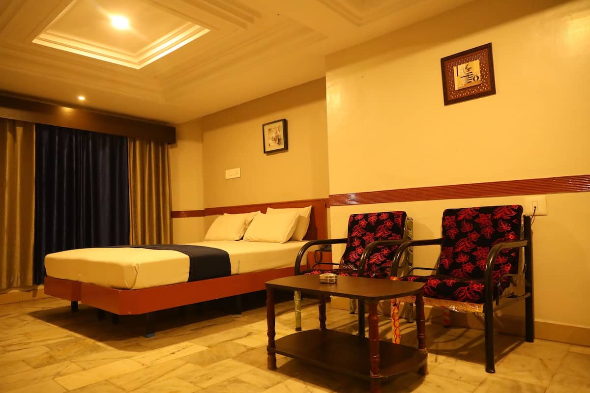 A hotel room with a bed, two chairs, a small table, and a ceiling light.