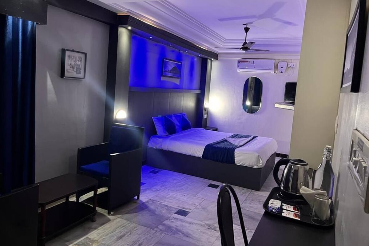 A modern hotel room with a bed, a desk, a chair, and a coffee machine.