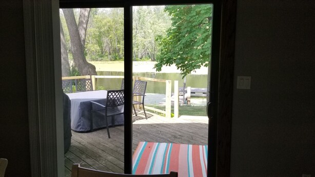 Vue depuis l’intérieur d’une pièce sur une terrasse extérieure avec une table et des chaises, un espace abrité et une terrasse en bois.