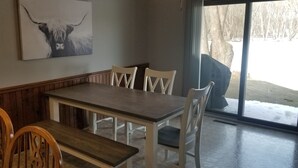 Un coin repas avec une table en bois et des chaises blanches, un grand tableau représentant un taureau accroché au mur, et une vue sur un paysage enneigé par une porte vitrée.