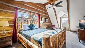 Ein Schlafzimmer in einer Blockhütte mit einem hölzernen Bett, einem Deckenventilator und einem großen Fenster.