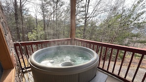 Ein Whirlpool auf einer Holzterrasse mit Geländer, umgeben von Bäumen.
