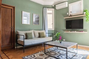 A living room with a sofa, a coffee table, a TV, and a window with curtains.