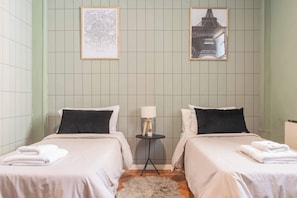 Ein Zimmer mit zwei Betten, einem kleinen runden Tisch mit einer Lampe und zwei gerahmten Bildern an der Wand.