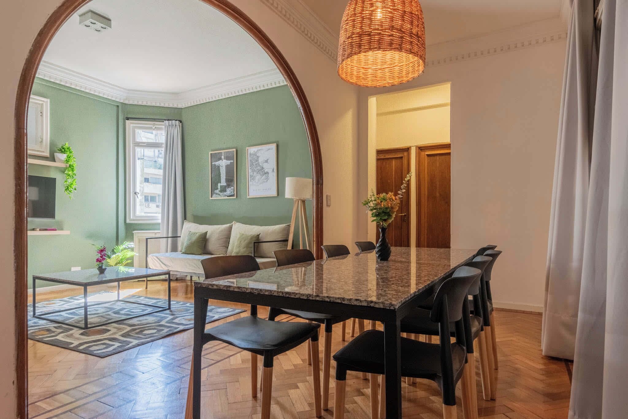 Un coin repas avec une table à plateau en verre, des chaises noires et un luminaire suspendu en fibres tressées.