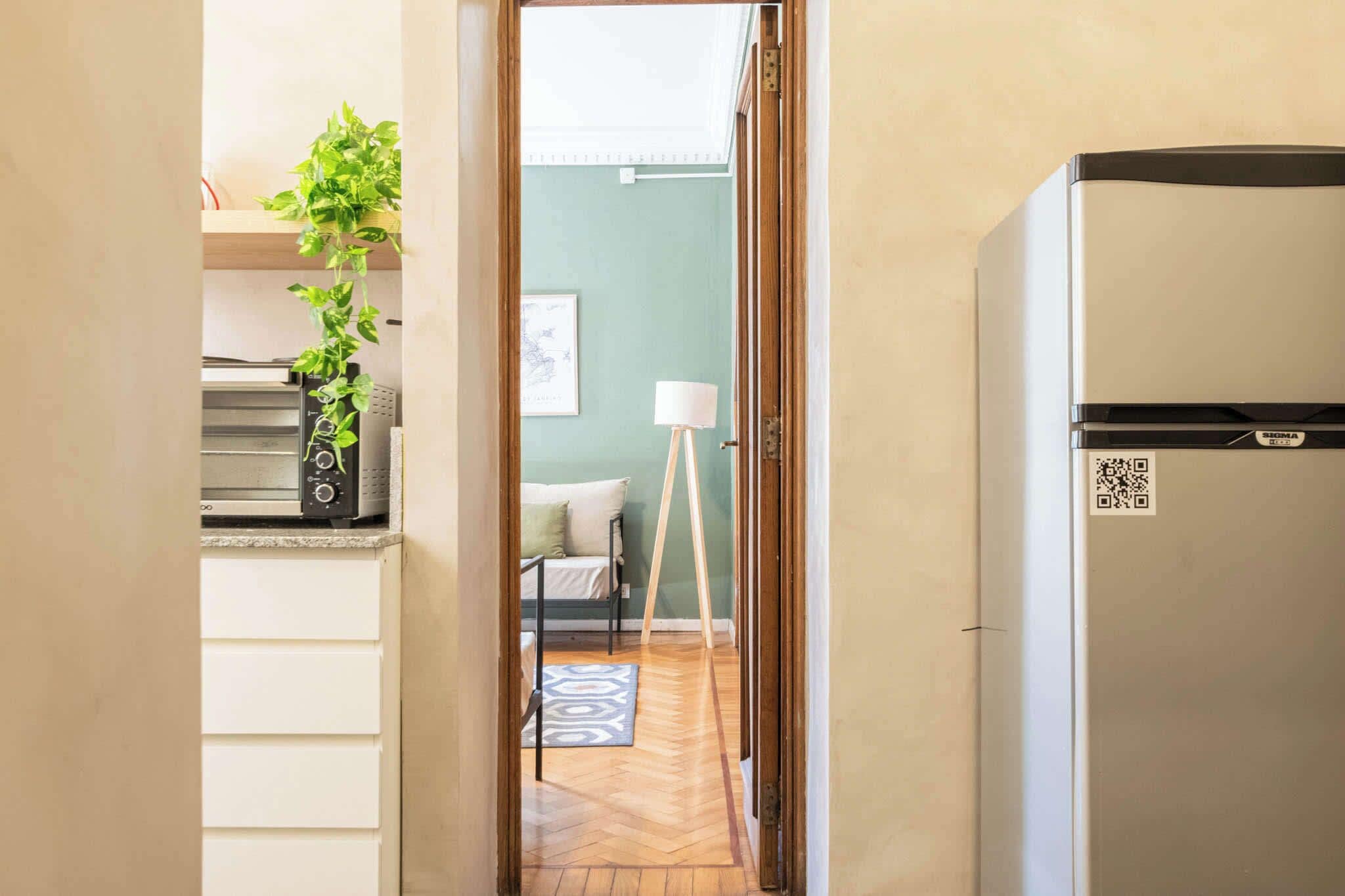 Corredor que dá para um quarto com cama, luminária de pé e planta.