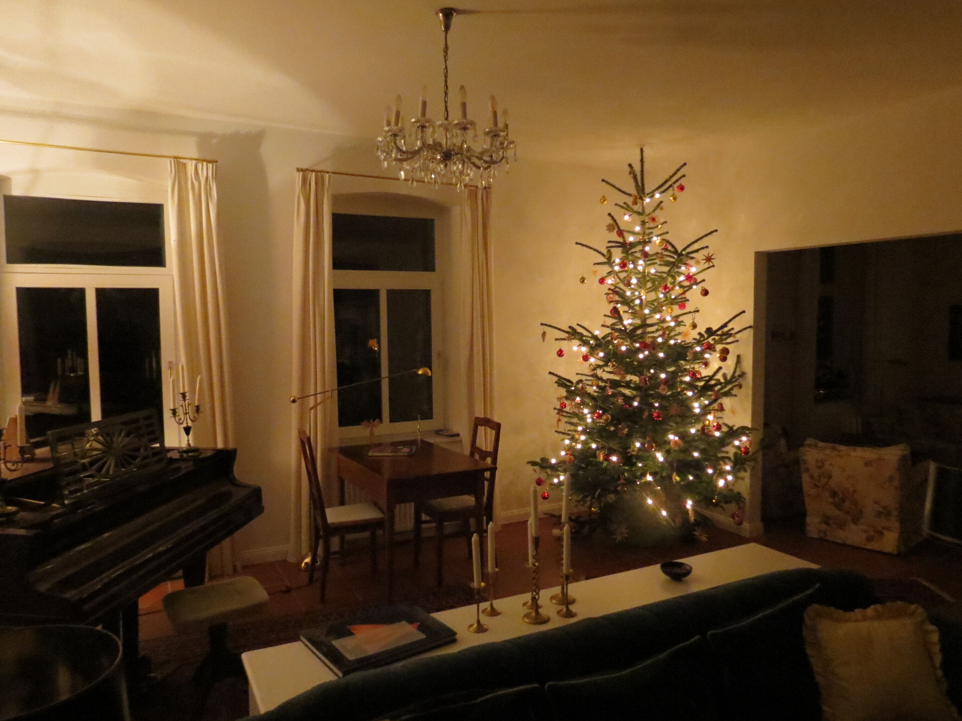 Ein gemütliches Wohnzimmer mit Weihnachtsbaum, einer Chandelieber, einem Klavier und einem Essbereich.