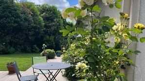Eine Terrasse mit Tisch und Stühlen, umgeben von üppiger Bepflanzung und blühenden Pflanzen.