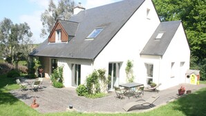 Ein Haus mit Satteldach, einer Terrasse mit Tisch und Stühlen sowie einem kleinen Garten.