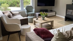 Ein modernes Wohnzimmer mit einer Couch, Sesseln, einem Couchtisch, einem Fernseher und einem Kamin.