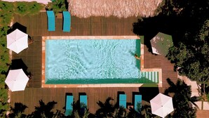 Eine Vogelperspektive auf einen rechteckigen Swimmingpool, umgeben von einer Holzterrasse, Liegestühlen und Sonnenschirmen.