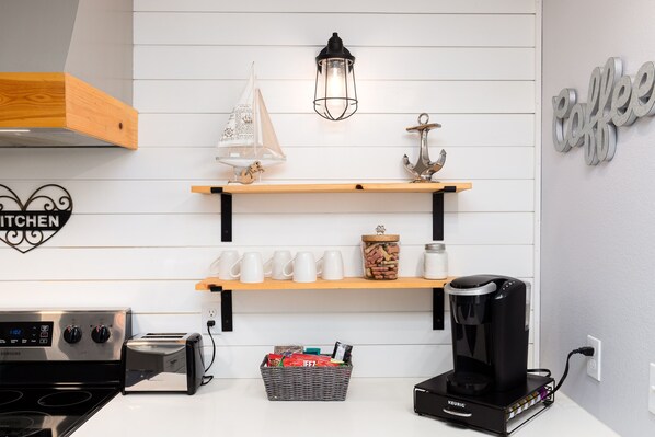 Een moderne keuken met een inbouwfornuis, een koffiezetapparaat en een plank met mokken en een decoratief zeilschip.
