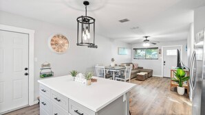 Una cocina moderna con armarios blancos, una isla central y un comedor con mesa y sillas.
