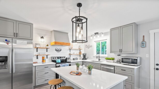 Una cocina moderna con una isla central, electrodomésticos de acero inoxidable y una lámpara colgante.