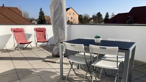 A rooftop terrace with a table and chairs, a potted plant, and two red chairs. - Apartment in detached house (Colmar)