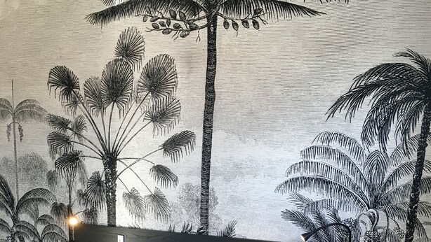 A bedroom with a bed, a headboard, a wall with a tropical plant mural, and a small round table with a plate. - Apartment in detached house (Colmar)