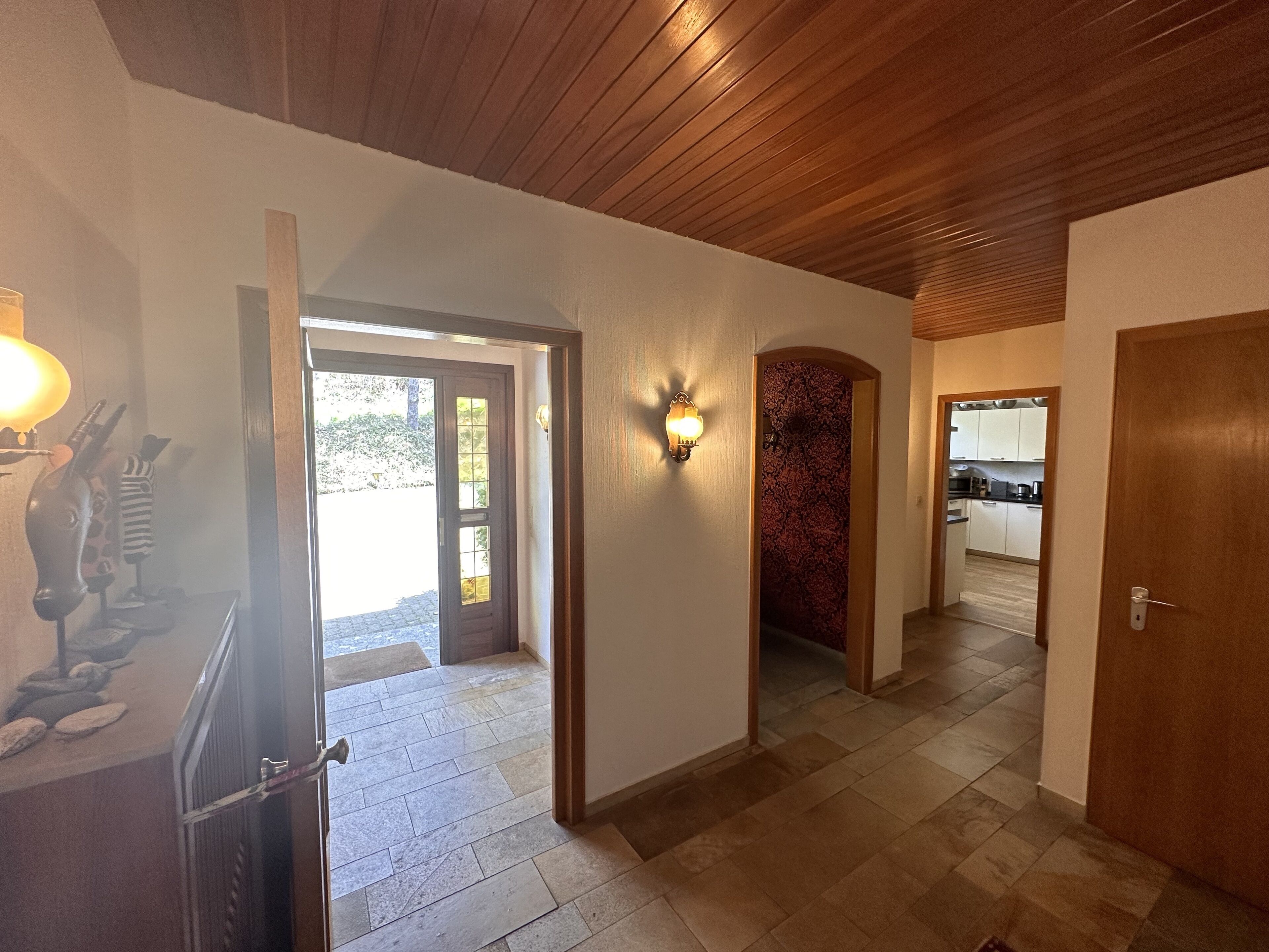 Un pasillo con techo de madera, suelo de baldosas de piedra y vistas a una cocina.