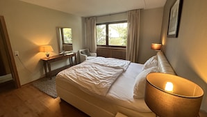 A hotel room with a bed, bedside lamp, desk, chair, and a window with curtains. - Villa close to Winterberg and Willingen (Bruchhausen)