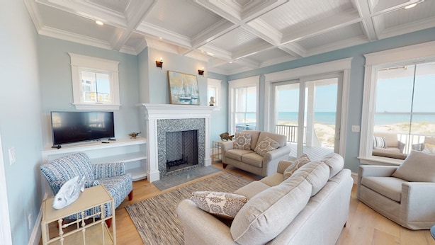 Ein geräumiges Wohnzimmer mit Fernseher, Kamin und Blick auf den Strand.