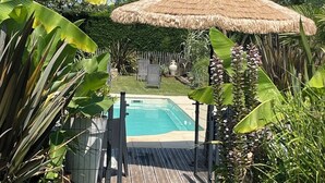 Un jardin à l’arrière de la maison avec une piscine, entouré d’une végétation luxuriante et agrémenté d’un gazebo à toit de chaume.