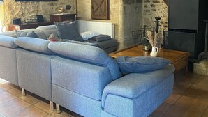 Un salon avec un mur en pierre, une cheminée, un grand canapé bleu et un téléviseur à écran plat fixé au mur.