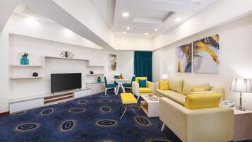 Une chambre d’hôtel moderne équipée d’un téléviseur à écran plat, d’un canapé, d’une table à manger et d’un tapis à motifs bleus.