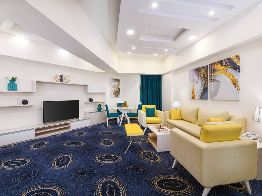 Une chambre d’hôtel moderne équipée d’un téléviseur à écran plat, d’un canapé, d’une table à manger et d’un tapis à motifs bleus.