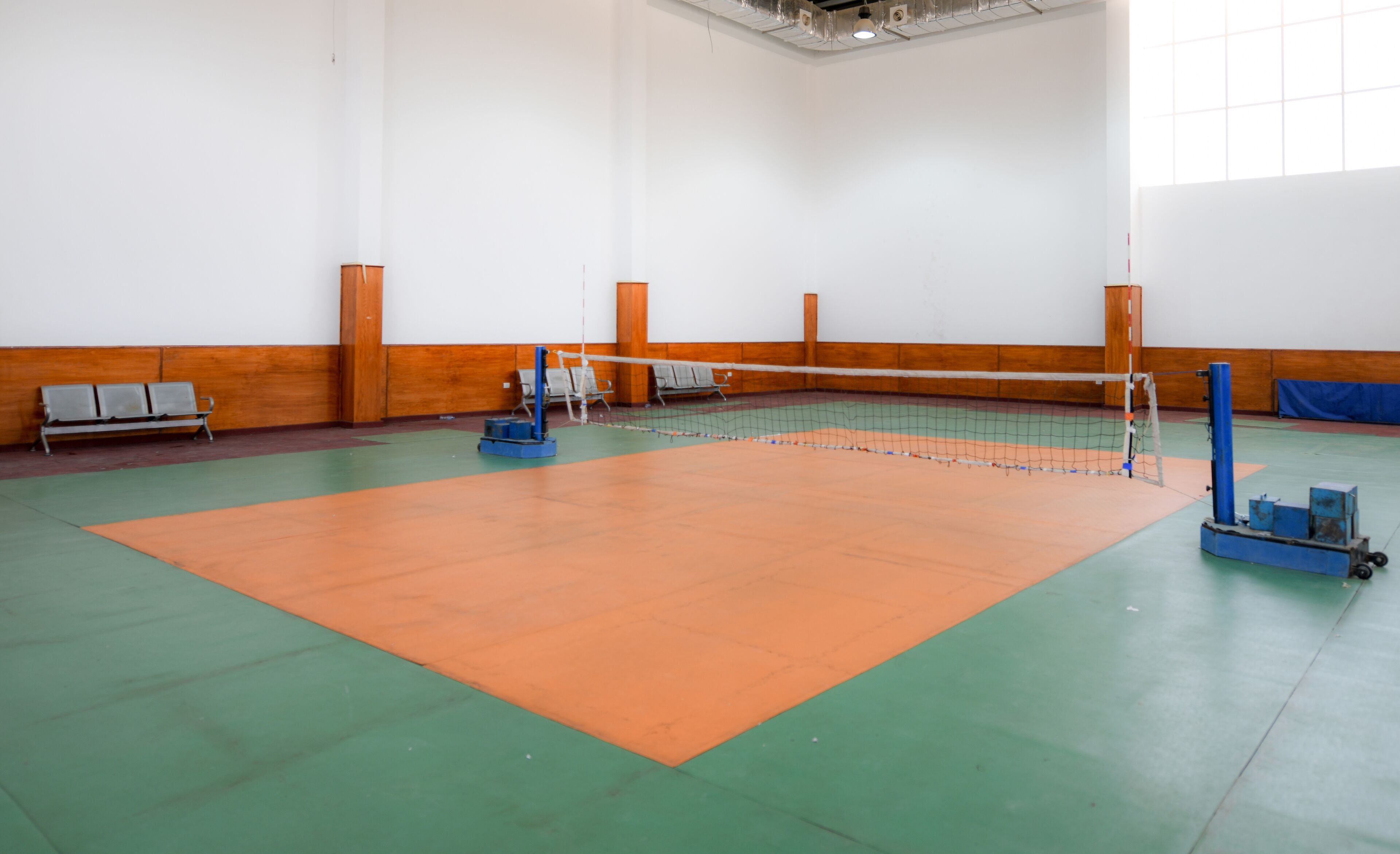 An indoor volleyball court with a net, benches, and a volleyball machine.