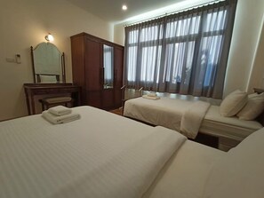 Ett hotellrum med två sängar, en garderob i trä, en spegel och ett fönster med gardiner.