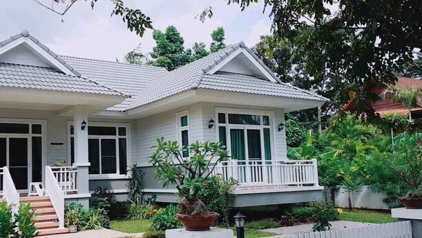 A two-story house with a covered porch, a small staircase, and a garden with various plants. - Resort house - 2 min walk to the beach (Amphoe Bang Saphan)