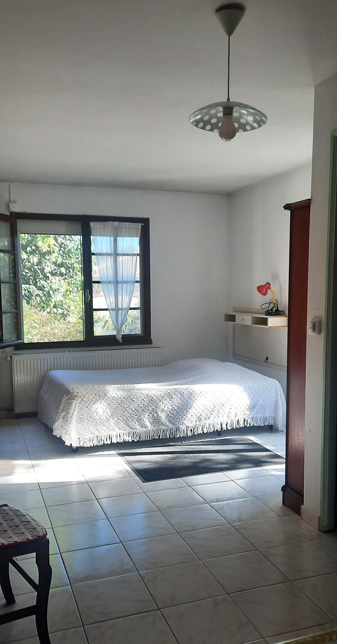 Una camera da letto con un letto, una finestra, un termosifone, una scrivania con una lampada e una sedia.
