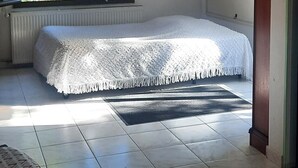 A bedroom with a bed, a window, a radiator, a desk with a lamp, and a chair.