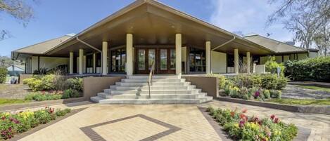 A modern building with a central entrance, a covered porch, and a landscaped garden area.