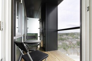 Un balcón con mesa y sillas, vista a una zona residencial y un ventanal grande.