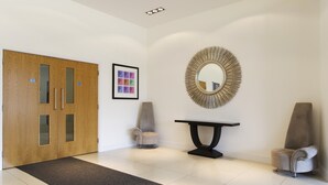 A modern lobby with a wooden door, a round mirror, a framed picture, and two armchairs. - KD Tower Abodebed (Hemel Hempstead)