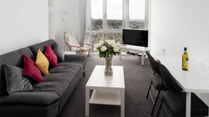 A modern living room with a grey sofa, a white coffee table, a TV, and a dining area with a white table and chairs. - KD Tower Abodebed (Hemel Hempstead)