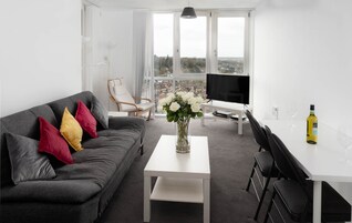Una sala de estar moderna con un sofá gris, una mesa de centro blanca, un televisor y un comedor con una mesa y sillas blancas.