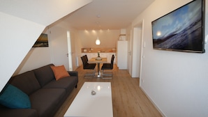 Un salon moderne avec un canapé marron foncé, une table basse blanche et un coin repas comprenant une table et des chaises en bois.