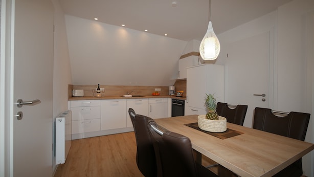 Une cuisine moderne avec des meubles blancs, un plan de travail en bois et un coin repas comprenant une table et des chaises.