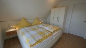Une chambre à coucher avec un lit, deux oreillers jaunes, une lampe de chevet, une armoire et une table de chevet.