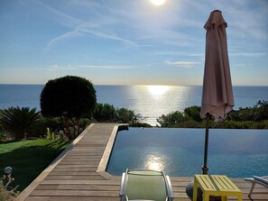 A wooden deck leading to a clear pool with a view of the sea and a sunset. - Villa with a pool and a 180° ocean view, 500 meters from the beach, air-conditioned (Roquebrune-sur-Argens)