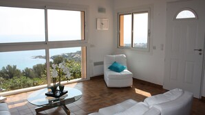 Ein großzügiger Wohnraum mit einem weißen Sofa, einem Glastisch und Meerblick.
