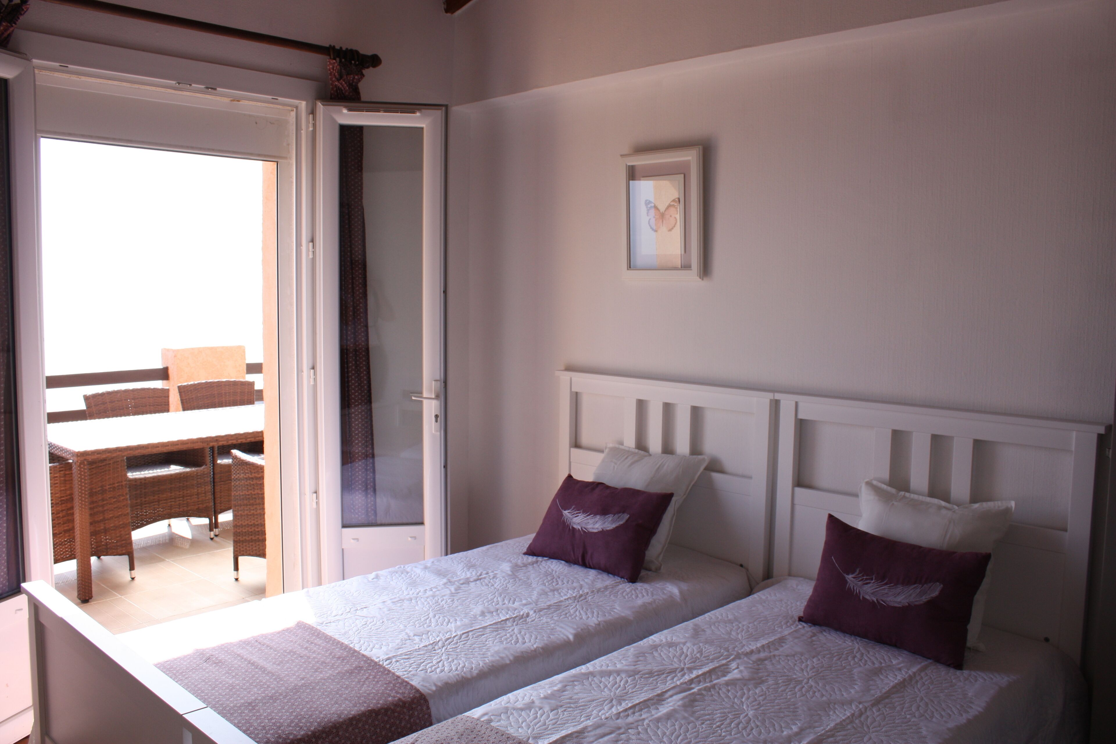A bedroom with two beds, a door leading to a balcony, and a framed picture on the wall.