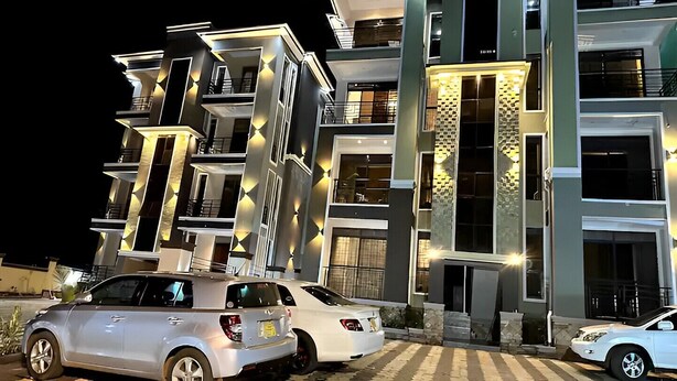 A modern multi-story building with illuminated architectural features and parked cars in front.
