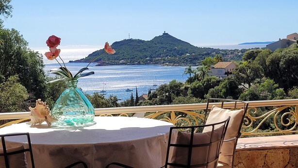 Ein Tisch mit einer Vase und einer Figur, mit Blick auf eine Küstenlandschaft mit Häusern und Grünpflanzen.