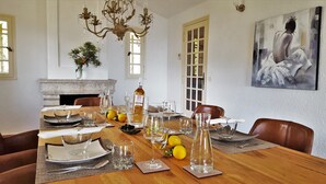 Ein Esszimmer mit Holztisch, gedeckt für sechs Personen, einer Chandelierleuchtre, einem Kamin und einem großen abstrakten Gemälde an der Wand.