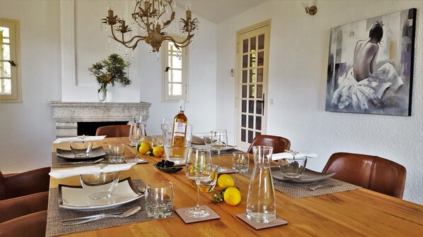 A dining room with a wooden table set for six, a chandelier, a fireplace, and a large abstract painting on the wall.