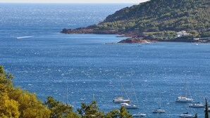 Blick auf die Küste mit mehreren Segelbooten, die vor einer felsigen Uferlinie mit spärlicher Vegetation ankern.