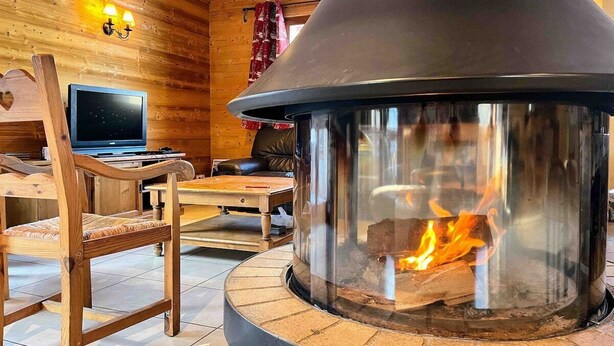 A cozy room with a stone fireplace, wooden walls, a comfortable chair, and a flat-screen TV. - WONDERFUL SPACIOUS CHALET IN BOURG D’OISANS - SLEEPS 10(*supplement available up to 16) (Le Bourg-d'Oisans)